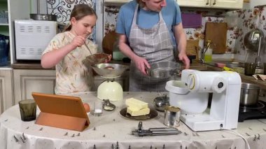 Önlüklü genç baba ve küçük kızı mutfakta birlikte yemek pişiriyorlar. Aile tatillerini paylaşırlar, yemek hazırlama ve sıcak bir yuva ortamında eğlenceli etkileşimlerle eğlenirler.