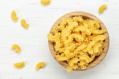 Kurutulmuş makarna, horoz istiridyesi. Tahta bir kasede ve beyaz bir masada makarna. Metin için boşluk.