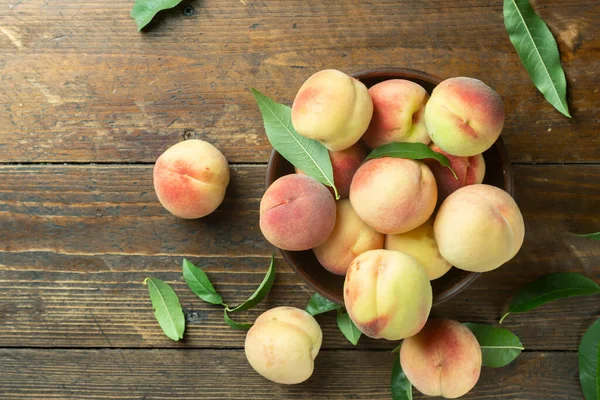Fresh sweet peaches on the wooden table, selective focus. Fresh ripe peaches with leaves in a bowl on a wooden background.