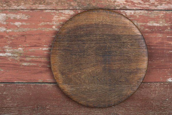 Circle cutting board on a red wooden table. Food preparation tool and kitchen utensils. Space for text.