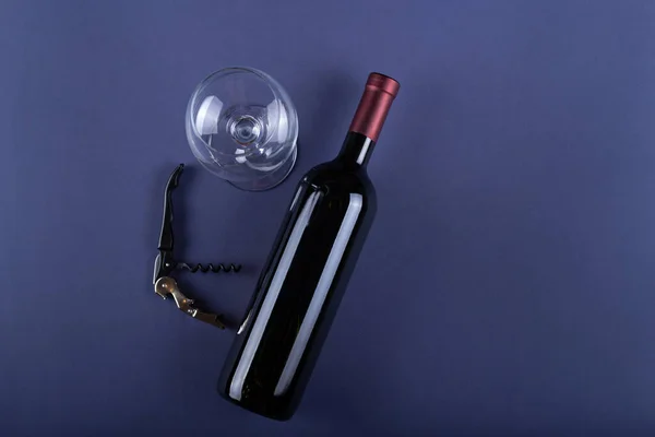 Red wine bottle without label, corkscrew and empty glass on purple paper background. Mockup drink with place for you label and text. Space for text.  Top view.