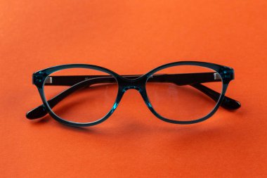 Stylish eyeglasses over orange background. Optical store, glasses selection, eye test, vision examination at optician, fashion accessories concept. Top view, flat lay