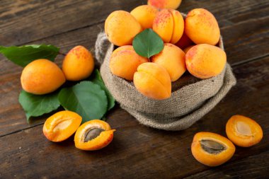 Ripe apricots and apricot leaves in a bag on a wooden background. Delicious fruits.