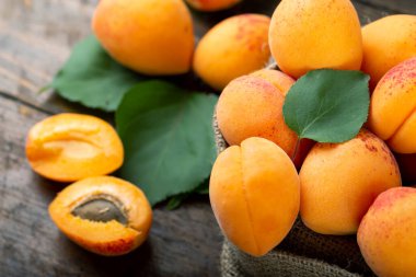 Ripe apricots and apricot leaves in a bag on a wooden background. Delicious fruits.