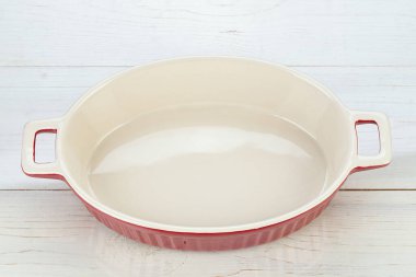 Red ceramic baking dish in wooden background. Empty oval baking dish for gratin. 