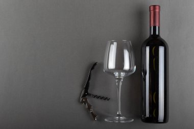 Mantarlı kırmızı şarap şişesi, tirbuşon ve gri arka planda boş şarap kadehi. Alkolik içki. Şarap yapma konsepti. Mesaj için yer var. Üst görünüm.