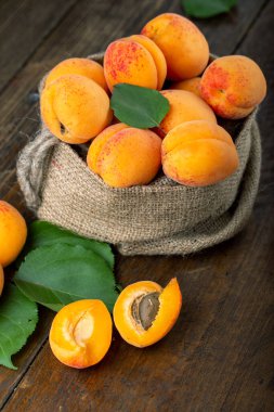 Ripe apricots and apricot leaves in a bag on a wooden background. Delicious fruits.