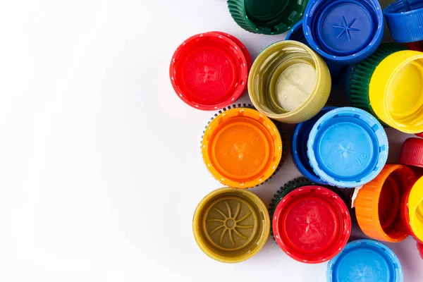 Multicolored plastic bottle caps are scattered on a white background. Plastic recycle place for text. Space for text.