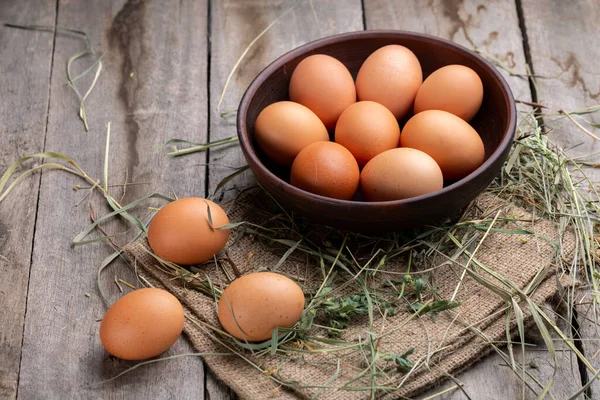 stock image Brown chicken eggs in a bowl on a background of hay and wooden boards. Farming concept.