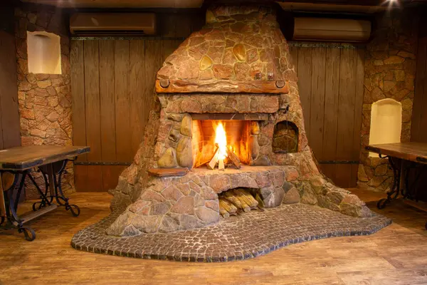 Old style stone fireplace. Wood burns in the fireplace with a blazing fire. Interior of the establishment.