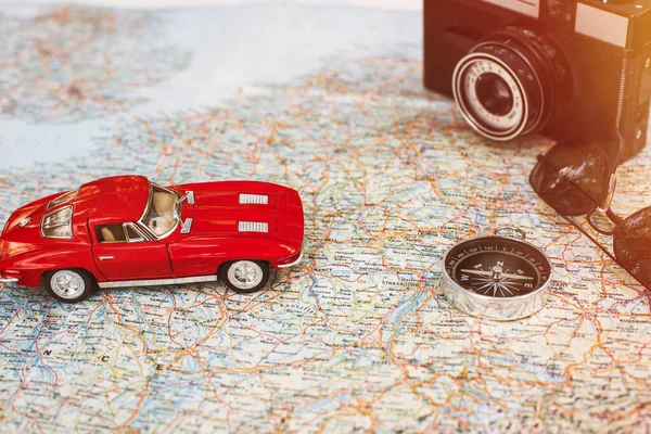 Traveling by car. Vintage red toy car, camera, compass and sunglasses lying on the map