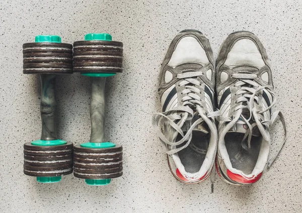 Vintage sport shoes and dumbbells on the floor, top view. Sport background