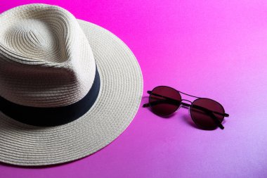 Sunglasses and straw panama hat isolated on a pink surface