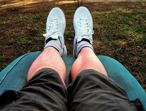 Mans legs and feet with shorts and sneakers lying on a sun lounger