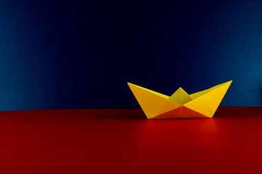 Katlanmış sarı origami teknesi mavi arkaplan ve kırmızı tabanlı.