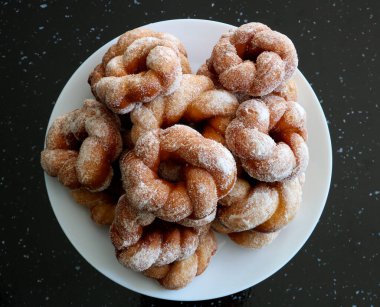Taze yapılmış şekerli çörekler, siyah granit bir yüzey üzerinde beyaz bir yemek tabağına istiflenmiş.