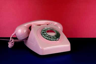 Pembe retro telefon izolü; mavi yüzey ve kırmızı arkaplan üzerine kuruludur.