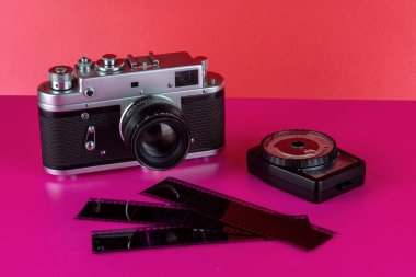 Vintage 35mm film camera on a pink surface and red background with vintage exposure meter and negatives clipart