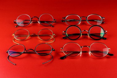 Kırmızı bir yüzeye yerleştirilmiş çeşitli eski moda metal gözlük çerçeveleri.