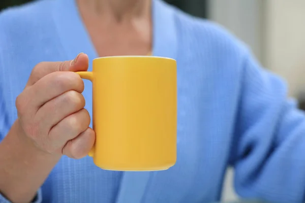 Yellow mug with coffee in the hands of a woman in a blue cardigan