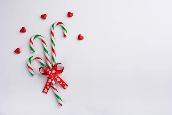Candy canes of red-green color, red heart shaped candies, red ribbon in the shape of a bow, light background