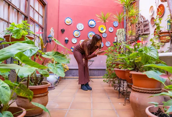 woman in pajamas bends down to see the plants in the garden, observes them carefully to take care of them