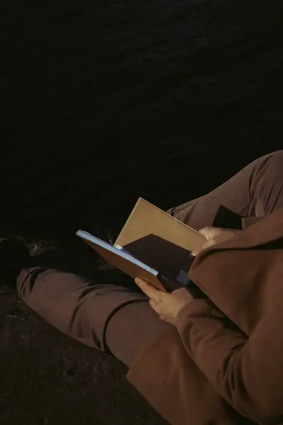 Adam geceleri sahilde kitap okuyor.