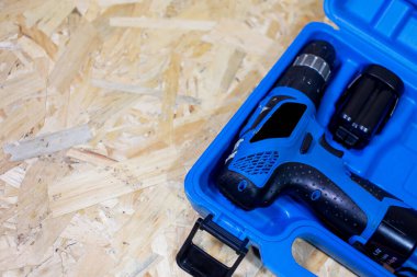 Kırmızı elektrikli matkap, siyah bir bavulun içinde, tahta bir masanın üzerinde.