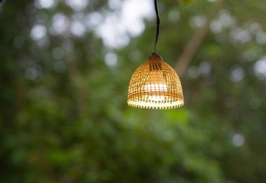 Elektrik lambası bambu dokumasından yapılmış, yeşil ağaç arka planı odak dışı..