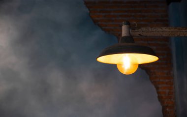 Duvardaki eski sarı parlak lamba, arka plan tuğla desenini gösteren alçı bir duvar..