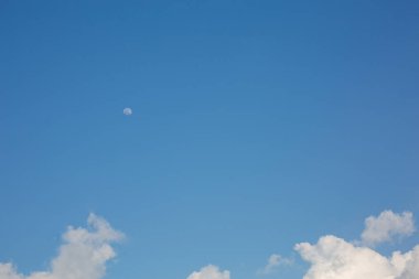 Beyaz bulutlu mavi bir gökyüzü ve gündüz vakti bir ay..