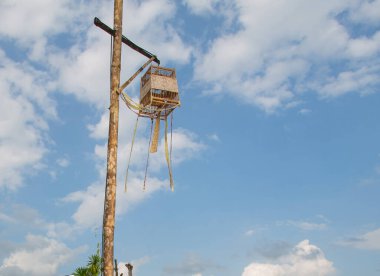 Bir kuş kafesi ahşap bir direğe asılı parlak mavi bir gökyüzü arka planına.