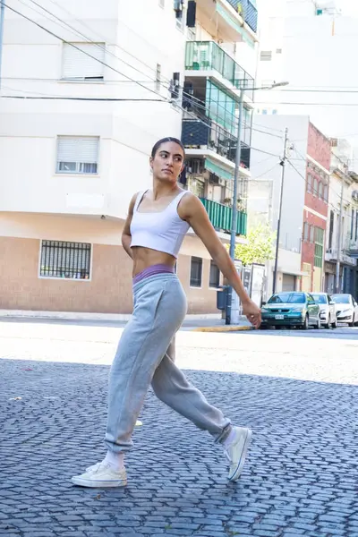 young fashionable woman crossing the street wearing a short white t-shirt and gray jogging pants. she has a fitness body.