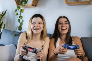 İki arkadaş gülüyor ve video oyunları oynuyor. Oturma odasında kanepede oturuyorlar. Birlikte vakit geçirmenin tadını çıkarıyorum. İkisi de beyaz tişört ve siyah şort giyiyor..