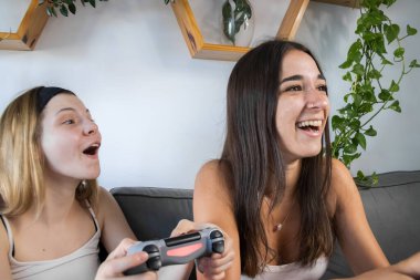 İki arkadaş gülüyor ve video oyunları oynuyor. Oturma odasında kanepede oturuyorlar. Birlikte vakit geçirmenin tadını çıkarıyorum. İkisi de beyaz tişört ve siyah şort giyiyor..