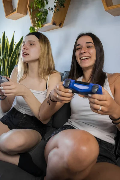best friends playing video games on the couch at home having fun and laughing. young woman with fair complexion and young woman with tan complexion