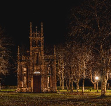 Gece vakti İberya 'da yapraksız ağaçlarla aydınlatılmış bir parkta kilise.