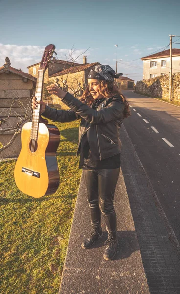 Genç bir kadın siyah bir gitarla yol kenarındaki bir duvara tünemiş başörtüsüyle