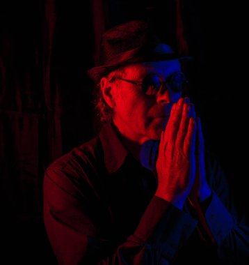 Şapkalı ve güneş gözlüklü bir adam, elleri gökyüzüne doğru karanlık bir yerde.