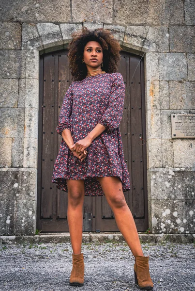 African-American woman with messy hair in front of a stone building door