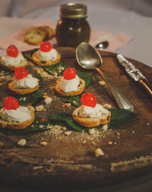 Kızarmış ekmekten yapılmış ahşap bir tabanda bir grup abur cubur beyaz krema ve üstünde kırmızı meyve.