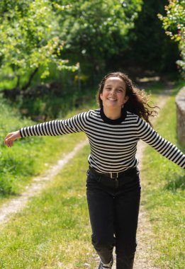 Genç kız kollarını açmış kırsal bir yolda koşuyor.