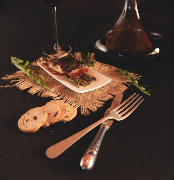 plate with baked food next to a container for wine and antique cutlery