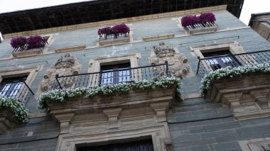 Renkli çiçeklerle dolu balkonları ve pencereleri olan bir ortaçağ evi cephesi