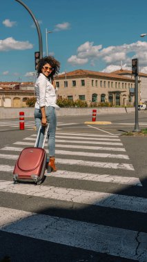 Güneş gözlüklü ve bavulu olan Afro-Amerikalı bir kadın.