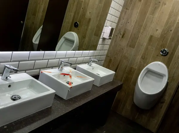 Public space for personal hand hygiene with mirror in which one of the sinks is broken