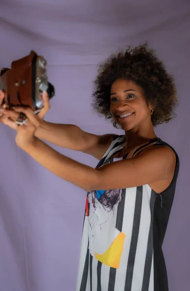 African American woman with an antique camera focuses in the distance as if it were a selfie