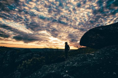 Gün batımında insan silueti yüksek bir yerde kırık bulutlu bahar gökyüzü ile gün batımını izliyor.