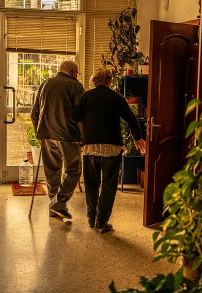 Yaşlı çift bitkilerin görüldüğü bir evin kapısına doğru gidiyor.