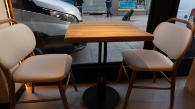 Bir masa ve iki boş sandalye bir dükkanın içinde sokağı görebileceğiniz bir pencerenin yanında.